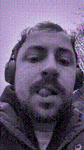 a selfie of a white person, wearing either headphones or a helmet, making an odd expression. the photo is edited to be colorized into a monochrome purple-ish color palette.