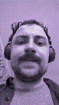 a selfie of a white person, wearing either headphones or a helmet, making an odd expression. the photo is edited to be colorized into a monochrome purple-ish color palette.