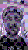 a selfie of a white person, wearing either headphones or a helmet, making an odd expression. the photo is edited to be colorized into a monochrome purple-ish color palette.