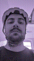 a selfie of a white person, wearing either headphones or a helmet, making an odd expression. the photo is edited to be colorized into a monochrome purple-ish color palette.